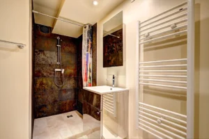 Salle de douche du loft à Paris 17 – Carrelage effet métal rouillé, meuble vasque moderne, miroir mural et sèche-serviettes blanc.