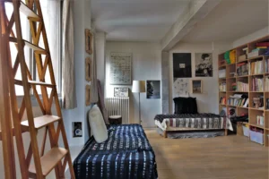 Grande chambre double dans un loft parisien, avec bibliothèque murale, lits séparés, poutre apparente et décoration artistique rue de Chabrol.