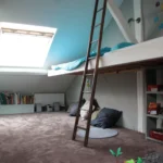 Chambre d’enfant en mezzanine dans un loft à Paris 10, avec aire de jeux au sol, échelle en bois, bibliothèque et grande fenêtre de toit apportant une lumière zénithale.
