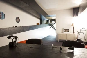 Couloir du niveau inférieur avec vue sur escalier métallique suspendu, éclairage naturel en fond.