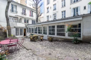 Cour végétalisée d’un loft à Paris 17 – Espace extérieur partagé avec mobilier naturel, arbres, pavés et façades d’immeubles parisiens.