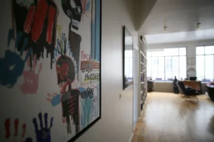 Couloir décoré d’une œuvre artistique colorée donnant sur le séjour lumineux d’un loft situé rue du Faubourg Saint-Denis à Paris 10ᵉ.