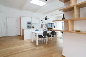 Cuisine ouverte et coin salle à manger, avec étagère en bois sur mesure, lumière naturelle et agencement fluide dans un loft à Paris 10.