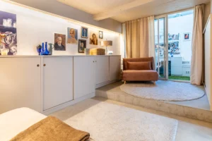 Pièce de détente cosy avec fauteuil en velours, éclairage tamisé et accès à un bureau vitré en second jour.