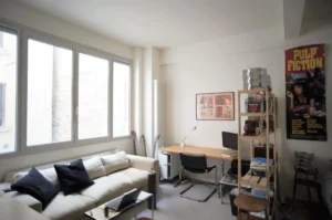 Espace polyvalent avec canapé, coin bureau et étagères, donnant sur une cour intérieure calme, dans un appartement à vendre Paris 10ᵉ rue Martel.