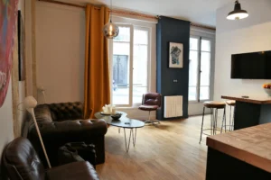Salon au style industriel dans un appartement à Montmartre Paris 18, avec mur en briques, œuvres d’art contemporain, canapé Chesterfield et parquet bois chaleureux.