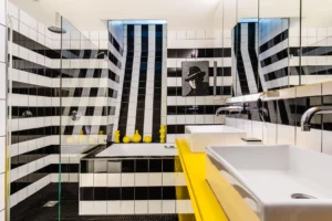 Salle de bains au design graphique noir et blanc, avec douche, baignoire, double vasque et plan jaune éclatant.