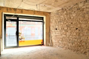 Vitrine sur rue du local commercial à rénover, avec mur en pierres apparentes, quartier Ménilmontant Paris 20ᵉ.