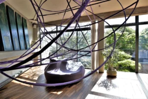 Détail d’un espace artistique lumineux avec vue arborée, sculpture suspendue violette et mobilier contemporain dans un loft à Bagnolet.