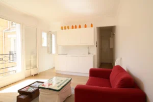 Pièce de vie lumineuse avec cuisine blanche ouverte et canapé rouge, appartement Paris 17ᵉ – rue Legendre.