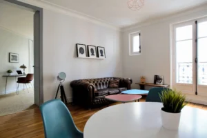 Salon au charme parisien avec canapé en cuir Chesterfield, sol en parquet et vue sur un espace bureau – appartement à vendre à Belleville, Paris 19ᵉ.