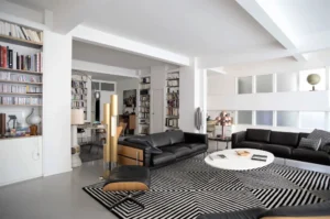 Vue d’ensemble du salon moderne avec canapés en cuir, tapis graphique noir et blanc et lumière naturelle, dans un appartement à vendre rue Martel Paris 10ᵉ.