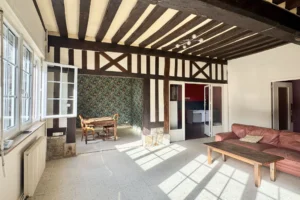 Séjour lumineux d’un appartement à vendre à Pont-l’Évêque, avec poutres apparentes, grande fenêtre et accès à la salle à manger.