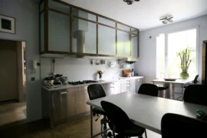 Cuisine industrielle d’un loft à Bagnolet, avec mobilier en acier brossé, verrière haute, table centrale et lumière naturelle traversante.