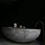 Salle de bain contemporaine dans un loft à Bagnolet, avec baignoire sculpturale en béton brut et robinetterie minimaliste en cuivre.