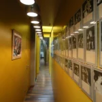 Couloir galerie dans un loft à Bagnolet, murs jaunes lumineux, suspensions contemporaines alignées et mur de photographies vintage encadrées.