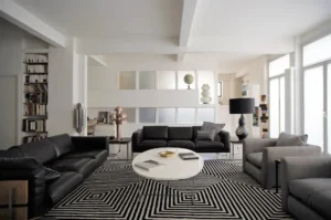 Grand salon lumineux avec canapés en cuir noir, fauteuils en tissu gris et tapis graphique, dans un appartement contemporain à Paris 10ᵉ, rue Martel.