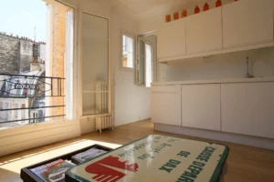 Cuisine blanche contemporaine avec vue sur les toits et murs en pierre, appartement Paris 17ᵉ – rue de Lévis.