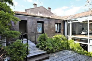 Accès extérieur du loft avec passerelle en bois, terrasse végétalisée et façade industrielle à Bagnolet, dans un environnement calme et verdoyant.
