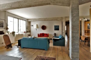 Salon chaleureux d’un loft ancien à Paris 10ᵉ avec poutres en béton brut, parquet patiné, canapés colorés et décoration vintage rue de Chabrol.