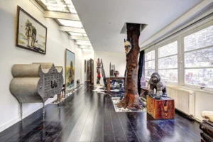 Loft lumineux à Paris 17 – Vue traversante sur un espace artistique avec œuvres tribales, grandes fenêtres sur cour et mobilier design dans un esprit galerie.