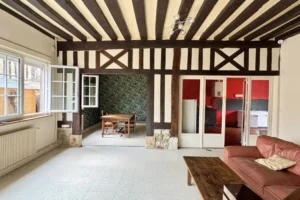Vue traversante sur la pièce de vie d’un appartement à vendre à Pont-l’Évêque, avec colombages, coin repas et cuisine séparée.