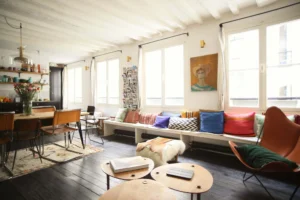 Salon parisien baigné de lumière avec banquette, coussins colorés et tableau rétro