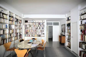Espace bureau et salle à manger avec grande bibliothèque murale, table en marbre et chaises design, dans un appartement rue Martel Paris 10ᵉ.
