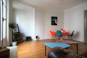 Espace repas moderne avec chaises colorées, parquet chaleureux et belle lumière naturelle – appartement à vendre à Belleville, Paris 19ᵉ.