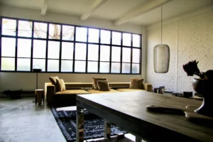 Espace de vie contemporain, associant une verrière sur toute la longueur, un canapé en velours, une table brute et un mur en brique blanche peint.