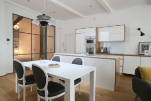 Vue sur la cuisine ouverte du loft, avec verrière industrielle donnant sur la chambre, coin repas élégant et finitions soignées.