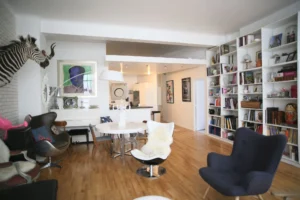 Vue d’ensemble d’un loft parisien avec cuisine ouverte, grande bibliothèque intégrée et mobilier design sur parquet clair, situé rue du Faubourg Saint-Denis à Paris 10ᵉ.