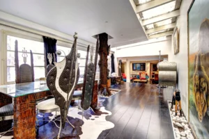 Salle à manger originale d’un loft à Paris 17 – Chaises sculpturales en métal, table en verre, sol en bois noir et plafond verrière dans un espace lumineux et artistique.