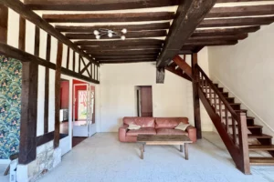 Salon d’un appartement à vendre à Pont-l’Évêque, avec escalier en bois, poutres apparentes et accès à l’étage.