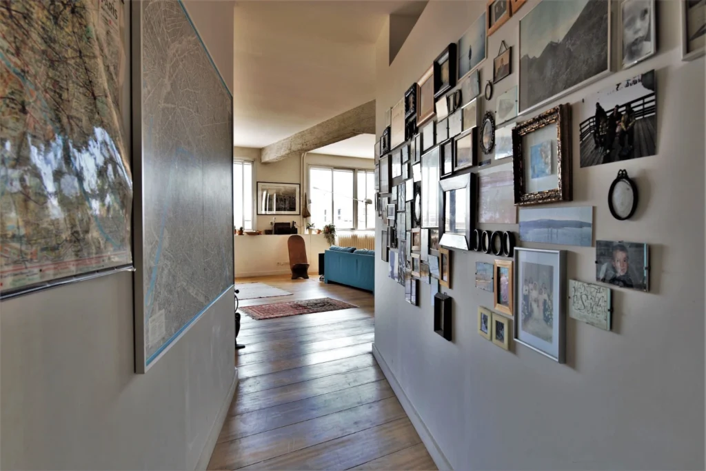 Couloir d’un loft à Paris 10ᵉ avec mur galerie de cadres, parquet ancien et vue sur l’espace de vie lumineux donnant sur rue de Chabrol.