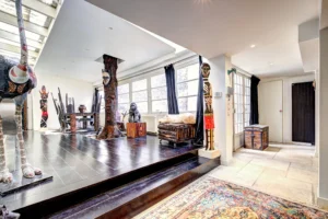 Entrée d’un loft à Paris 17 – Sol en pierre claire, sculptures ethniques, escalier en bois sombre et ambiance artistique lumineuse.