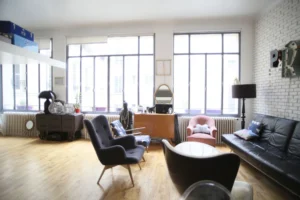 Salon cosy avec verrière, parquet en bois clair et fauteuils design dans un loft lumineux situé rue du Faubourg Saint-Denis à Paris 10ᵉ.