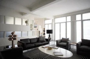 Salon moderne baigné de lumière naturelle avec canapés en cuir et fauteuils en tissu, grandes baies vitrées, dans un appartement à vendre à Paris 10ᵉ, rue Martel.