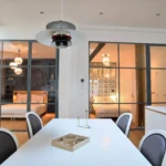 Deux chambres séparées par une verrière, avec éclairage suspendu, murs décorés et mobilier élégant dans un loft à Paris 10.
