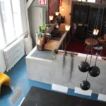 Vue en plongée sur une cuisine de loft à Paris 10, mêlant plan de travail en bois, murs en béton brut, suspensions noires et décoration créative dans un esprit industriel.