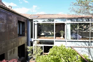 Façade vitrée d’un loft contemporain à Bagnolet, avec structure métallique, vue traversante sur le séjour et végétation en premier plan.
