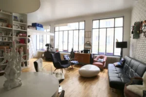 Grande pièce de vie lumineuse avec verrière, bibliothèque murale et mobilier éclectique dans un loft situé rue du Faubourg Saint-Denis à Paris 10ᵉ.