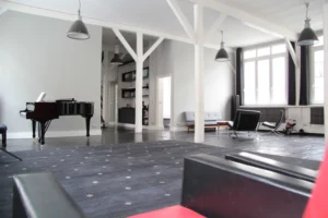 Espace salon lumineux avec piano à queue, bibliothèque intégrée, fauteuils design et parquet noir, dans un loft familial du 10ᵉ arrondissement à Paris.