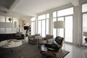 Coin salon raffiné avec fauteuil Eames, lampes design et grande baie vitrée, dans un appartement lumineux à vendre à Paris 10ᵉ, rue Martel.