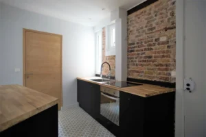 Cuisine ouverte au style industriel avec mur en briques, plan de travail en bois et électroménager intégré – appartement à vendre à Paris 19ᵉ, quartier Belleville.