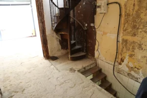Accès au sous-sol du local commercial via escalier, murs à rénover et installation électrique apparente.
