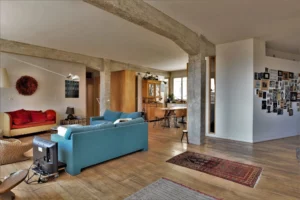 Vue dégagée sur l’espace ouvert du loft avec salon, salle à manger et cuisine, poutres béton, parquet ancien et décoration murale personnalisée, Paris 10ᵉ.