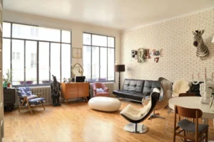 Salon ensoleillé avec mur en briques blanches, mobilier arty et grandes fenêtres dans un loft situé rue du Faubourg Saint-Denis à Paris 10ᵉ.
