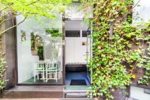 Accès à la terrasse depuis la cuisine, bordé de végétation grimpante et baies vitrées offrant un lien fluide intérieur/extérieur.