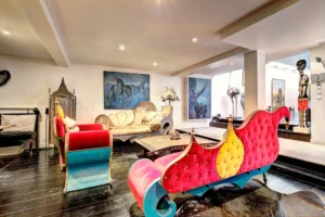 Salon artistique d’un loft à Paris 17 – Canapés colorés, tableaux contemporains, mobilier sculptural et ambiance chaleureuse dans un espace singulier.